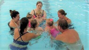 five adults giving four young children swimming lessons