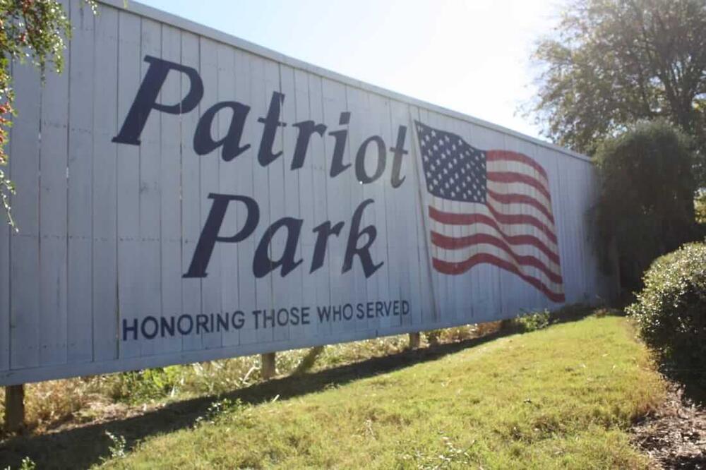 a large wooden sign with an American flag that says patriot park honoring those who served